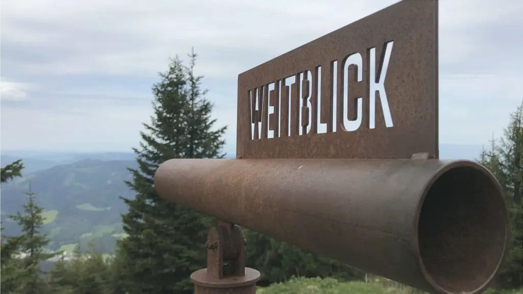 Ein Rohr symbolisiert ein Fernglas und ermöglicht den genauen Blick auf das Panorama im Hintergrund. Auf dem Rohr ist der Schriftzug "Weitblick" zu lesen.